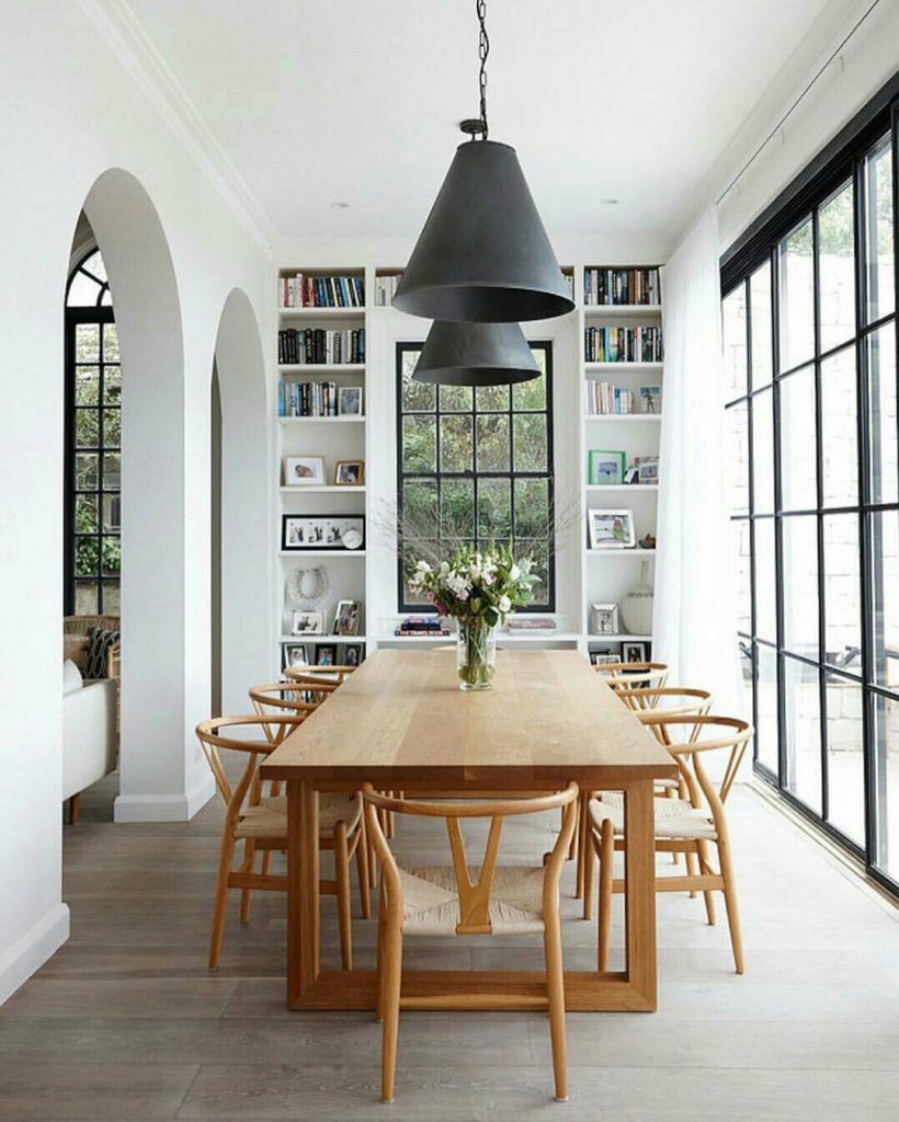 Beautiful dining room with wishbone chairs black light fixtures and black French doors / windows