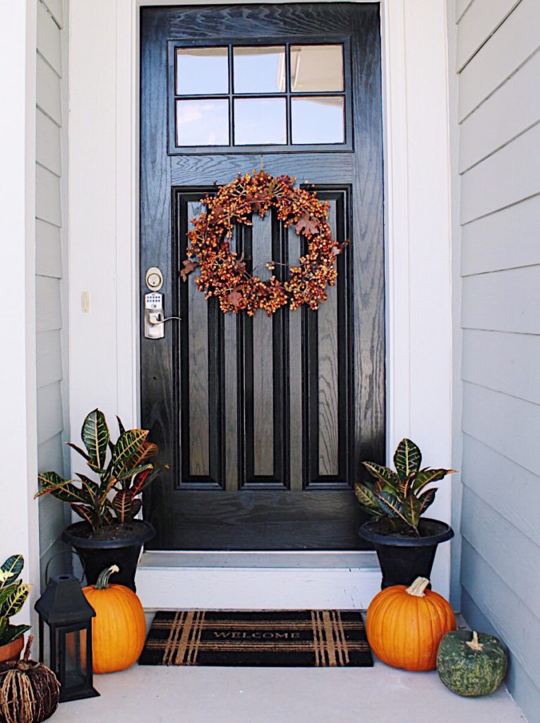 Fall front porch decor with classic orange and black urns filled with green plants - jane at home